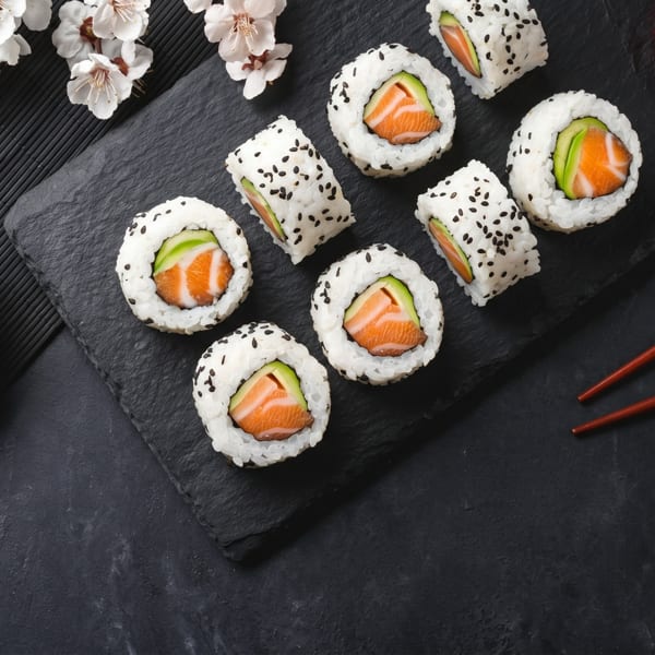 Salmon and avocado sushi rolls with soy sauce, pickled ginger, chopsticks, and cherry blossoms.