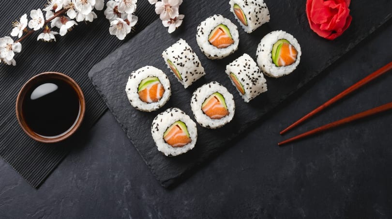 Salmon and avocado sushi rolls with soy sauce, pickled ginger, chopsticks, and cherry blossoms.