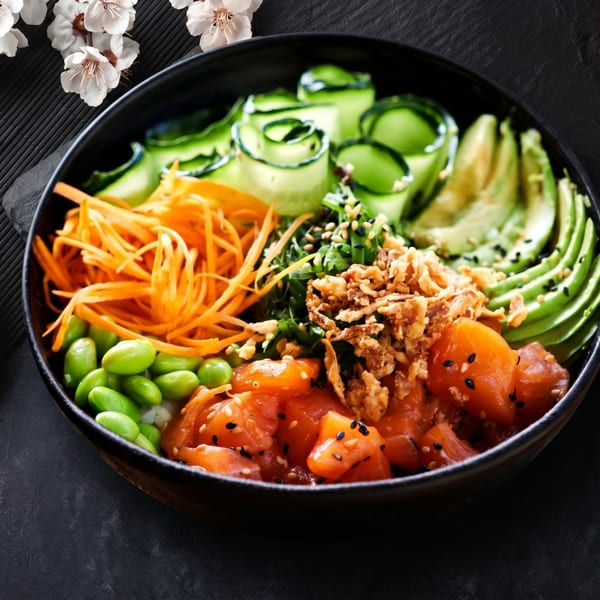 Colorful poke bowl with salmon, avocado, cucumber, carrots, edamame, and crispy onions.