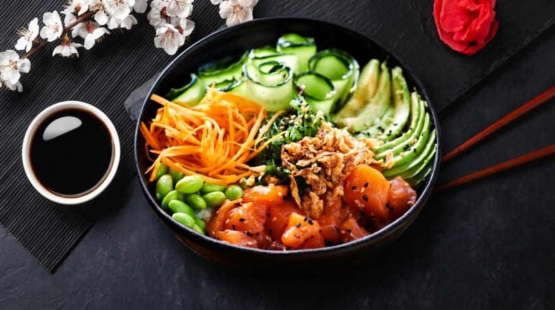 Colorful poke bowl with salmon, avocado, cucumber, carrots, edamame, and crispy onions.