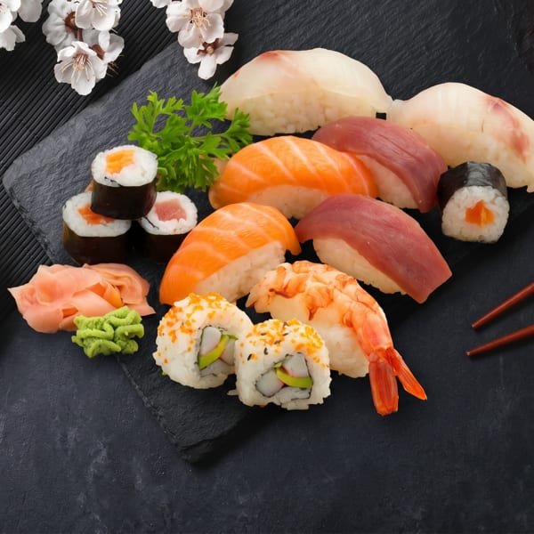 Assorted sushi and sashimi platter with soy sauce, ginger, wasabi, and chopsticks on a dark mat.