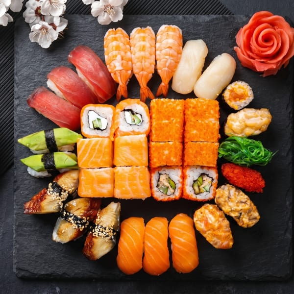 Assorted sushi and sashimi platter with soy sauce, chopsticks, and cherry blossoms on a dark slate.