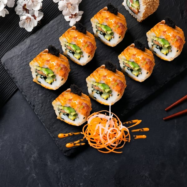 Top-down view of sushi rolls with orange sauce and black caviar, soy sauce, and chopsticks.